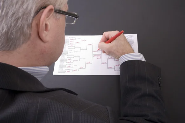 March Madness Businessman Crossing Out Teams on Bracket Stock Picture