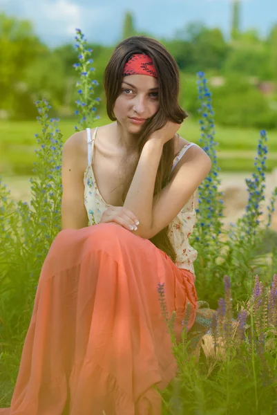Jonge mooie tiener meisje zit tegen bloem achtergrond — Stockfoto