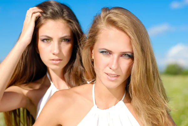 Deux jeunes femmes heureuses avec un maquillage lumineux sur fond bleu ciel — Photo