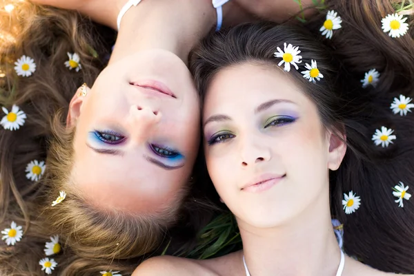 Two beautiful women lying head to head with camomile flowers in — Stock Photo, Image
