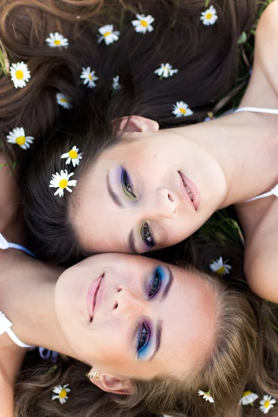 Dos hermosas mujeres tumbadas cabeza a cabeza con flores de manzanilla en — Foto de Stock