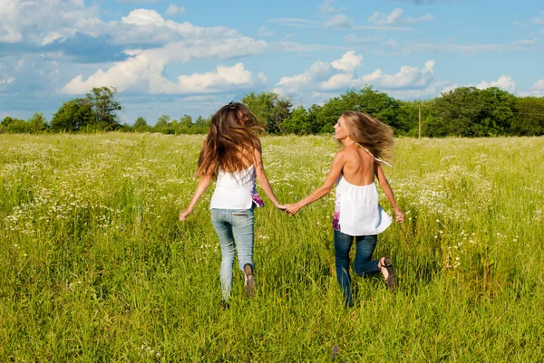 Two happy young women running on green field under blue sky — Stock Photo, Image