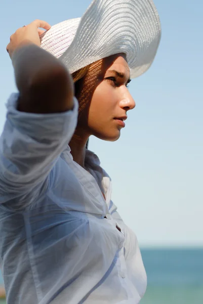 Mujer joven descansando junto al mar y vistiendo sombrero blanco — Foto de Stock