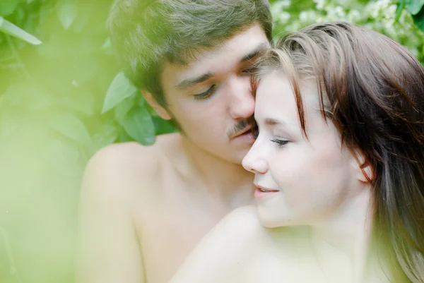 Giovane coppia felice che abbraccia teneramente tra foglie verdi — Foto Stock