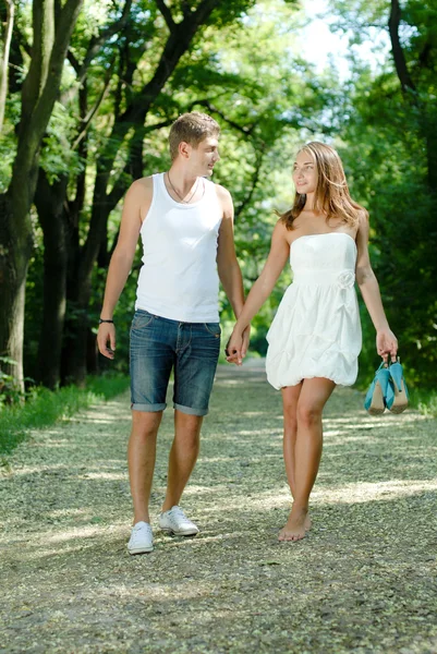 Joven feliz pareja caminando en verde parque cogido de la mano — Foto de Stock