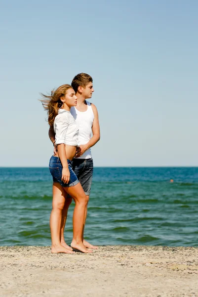 Szczęśliwa młoda para stoi na lato wietrzny dzień przez błękitne morze — Zdjęcie stockowe
