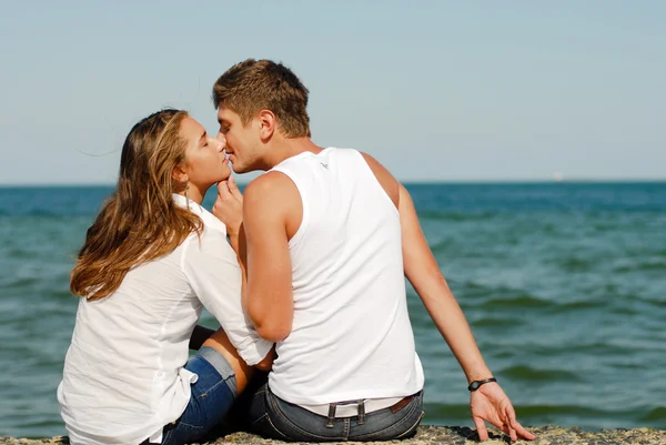 Gelukkige jonge paar kussen door blauwe zee over blauwe hemelachtergrond — Stockfoto