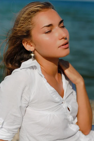 Young beautiful woman sitting by blue sea on windy summer day — Stock Photo, Image