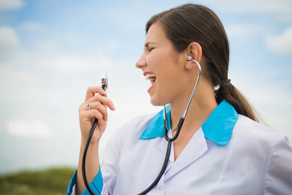 Doctora joven cantando en estetoscopio sobre fondo de cielo azul —  Fotos de Stock