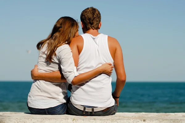 Happy young couple sitting by blue sea over blue sky background — Stock Photo, Image