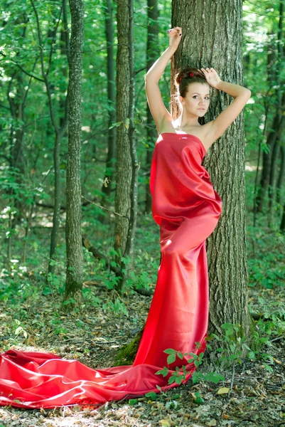 Jonge mooie vrouw in rode jurk in groene bossen — Stockfoto