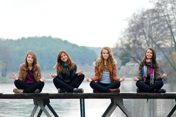 Quattro ragazze della scuola sedute sul ponte sul fiume — Foto Stock