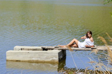 iskelede nehir ya da göl üzerinde oturan beyaz elbiseli mutlu genç kadın