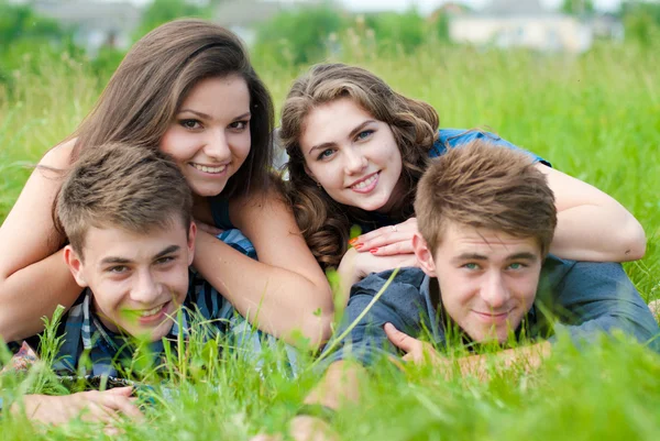 Cuatro amigos adolescentes felices acostados juntos en la hierba verde al aire libre Fotos De Stock Sin Royalties Gratis