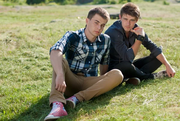 Två unga män sitter tillsammans på grönt gräs — Stockfoto