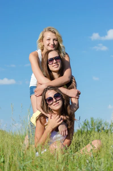 Tre glada teen tjejer embracing mot blå himmel — Stockfoto