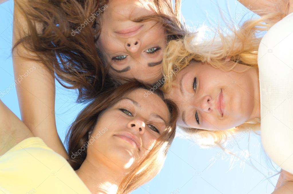 Three happy teen girls looking down against blue sky
