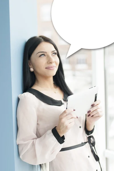 Lachende jonge zakenvrouw gebruiken, tablet pc terwijl je ontspannen in de buurt van venster op haar kantoor — Stockfoto