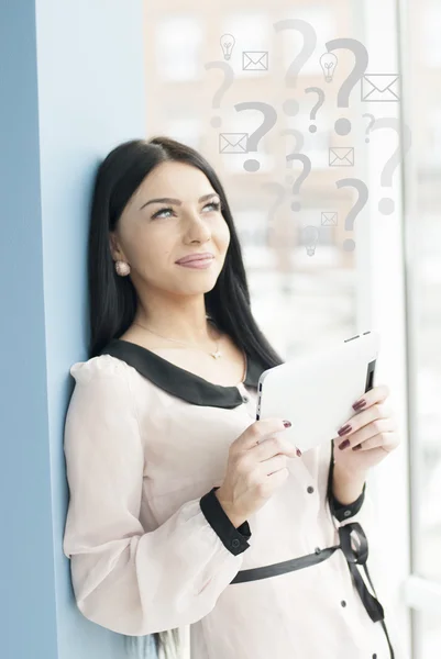 Усміхнена молода бізнес-леді використовує планшетний ПК, стоячи розслабленим біля вікна в її офісі — стокове фото