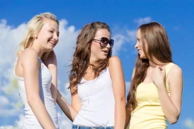 Three happy teen girls embracing against blue sky