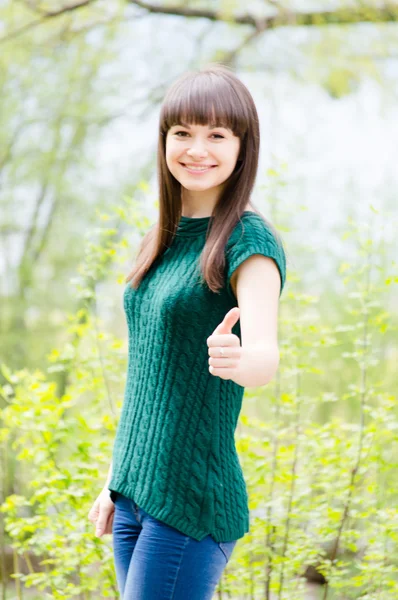 Красивая молодая женщина в вязаной зеленой блузке показывает большие пальцы вверх — стоковое фото
