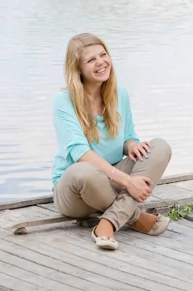 Mujer joven sentada en el muelle y sonriendo —  Fotos de Stock