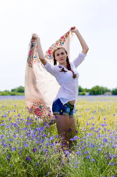 Joven mujer sonriente de pie en el campo de trigo amarillo sosteniendo un chal blanco en el viento — Foto de Stock