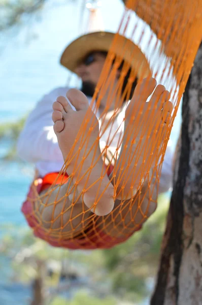 Mężczyzna w kapeluszu w hamaku na drzewo sosny na Krymie w letni dzień — Zdjęcie stockowe