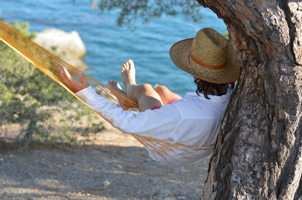 Man in hoed in een hangmat op naaldboom op de Krim een zomerdag — Stockfoto