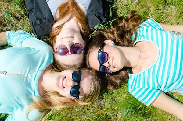 Три счастливые девочки-подростки лежат на зеленой траве в солнечных очках — стоковое фото