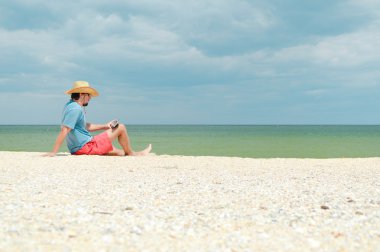 tablet bilgisayar ile deniz kenarında oturan ve oturan genç adam