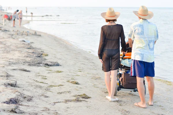 Jovem família feliz com carrinho de bebê andando na praia de areia — Fotografia de Stock