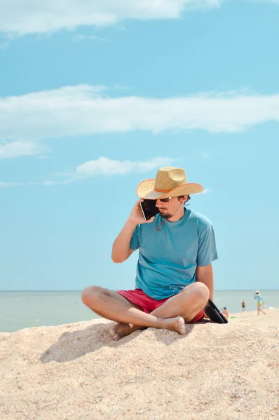 Tablet bilgisayar ile deniz kenarında oturan ve oturan genç adam — Stok fotoğraf