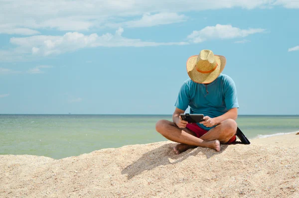 Jovem sentado à beira-mar com computador tablet e descansando — Fotografia de Stock