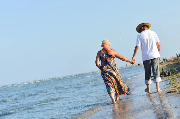 Happy mature couple walking at seashore sandy beach and holding hands — Stock Photo, Image