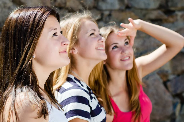 Tre glada teen girl vänner tittar tillsammans i en riktning — Stockfoto
