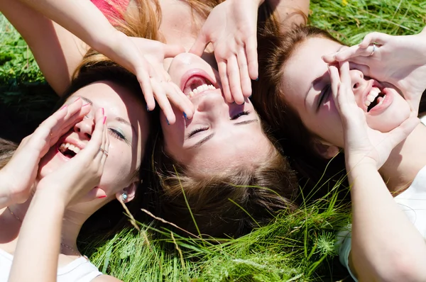 Tre glada teen tjejer liggande på grönt gräs titta in i himlen och hålla händer — Stockfoto