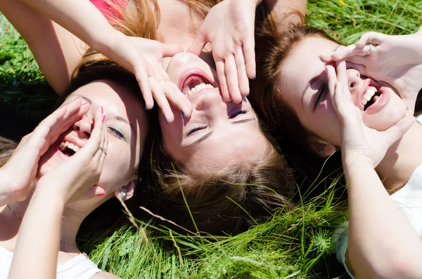 Three happy teen girls lying on green grass looking into sky and holding hands Royalty Free Stock Images