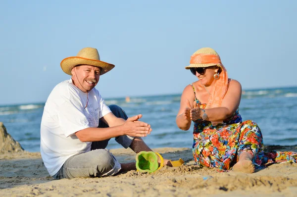 Happy mature couple sitting at seashore on sandy beach — Stock Photo, Image