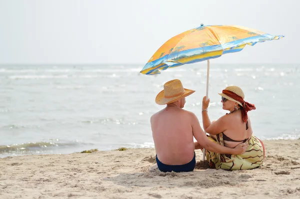 Happy mature couple sitting at seashore on sandy beach — Stock Photo, Image