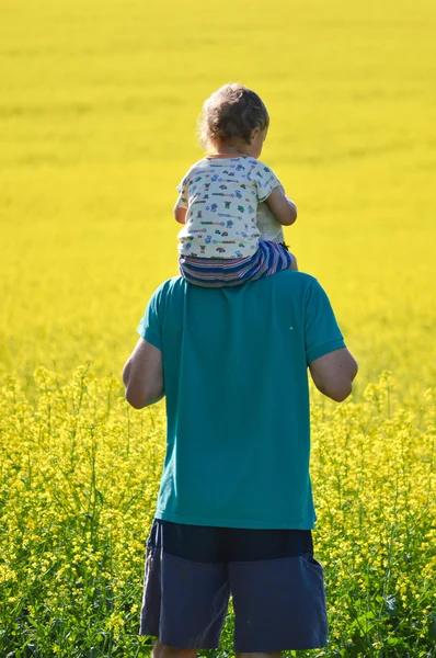 Father and son looking on rapeseed field on summer day — Stock Photo, Image
