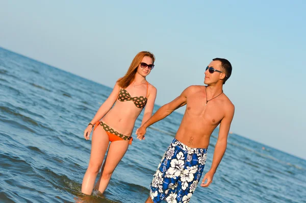Молодая счастливая пара идет, держа руки на берегу моря — стоковое фото