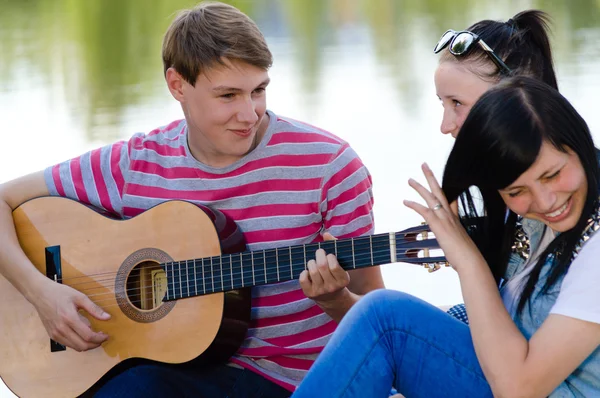 Tres amigos adolescentes felices tocando la guitarra en el verde parque de verano —  Fotos de Stock