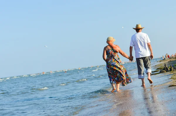 Szczęśliwy starsza para spaceru morza piaszczystej plaży i trzymając się za ręce — Zdjęcie stockowe