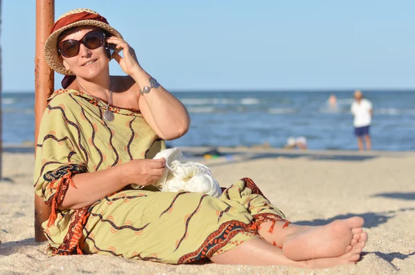 Kumsalda oturuyor ve cep telefonda konuşurken mutlu olgun kadın — Stok fotoğraf
