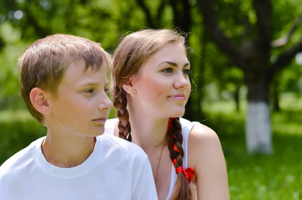 Mladý bratr a starší sestra sedí v zelené letní zahrada — Stock fotografie
