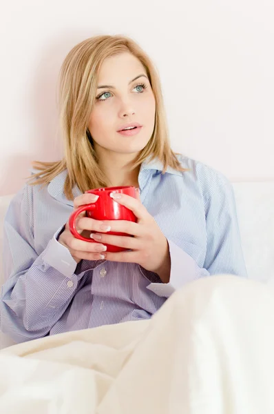 Hermosa mujer joven sonriente feliz en la cama sosteniendo taza de bebida caliente o agua mirando hacia arriba — Foto de Stock