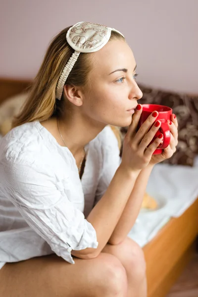 Mujer con una máscara para dormir y una taza de bebida caliente — Foto de Stock