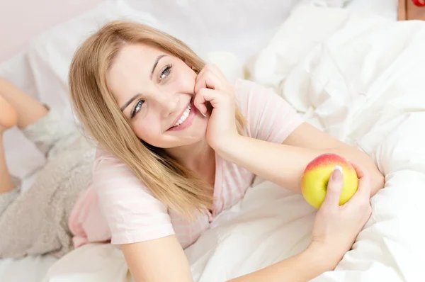 Kvinna i sängen med saftigt äpple i händer — Stockfoto