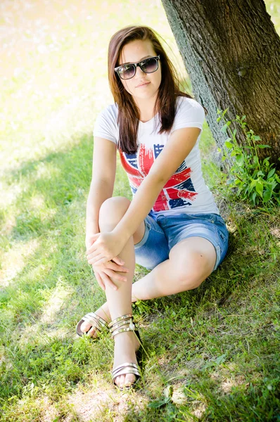 Menina sentada perto da árvore no parque — Fotografia de Stock